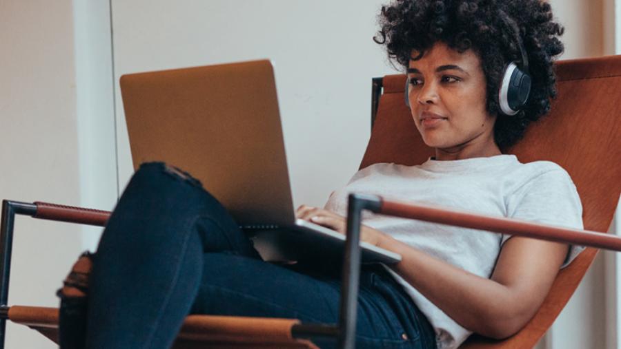 woman sitting in a chair looking at a laptop and wearing headphones